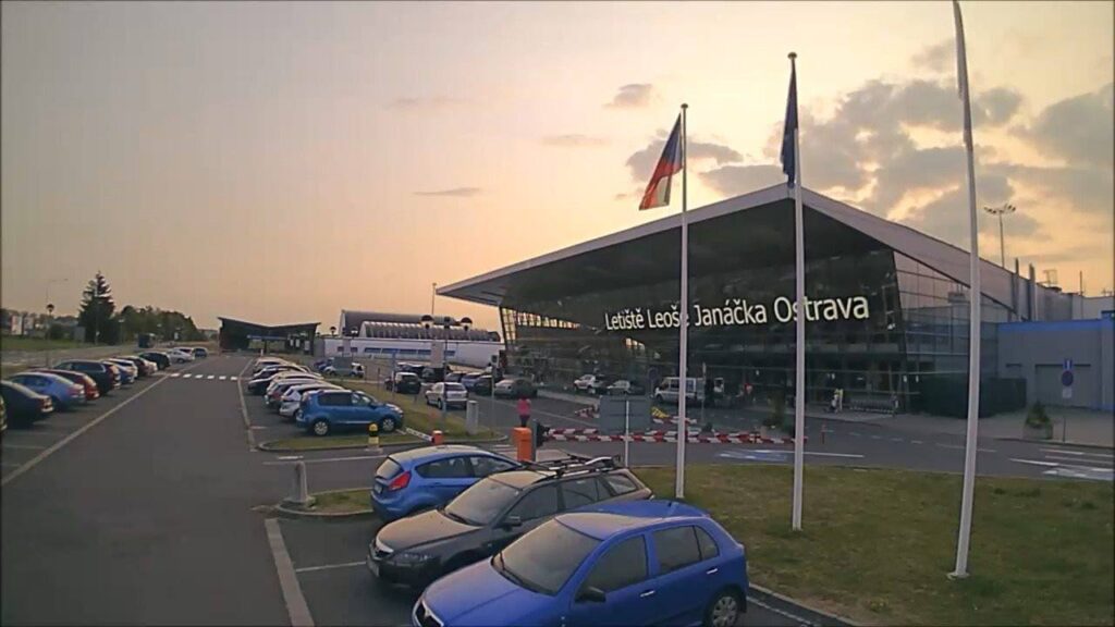 Terminál Letiště Leoše Janáčka Ostrava s parkovištěm a vlajkami při západu slunce