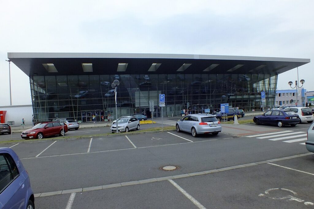 Prosklená budova hlavního terminálu Letiště Leoše Janáčka Ostrava s parkovištěm před vstupem